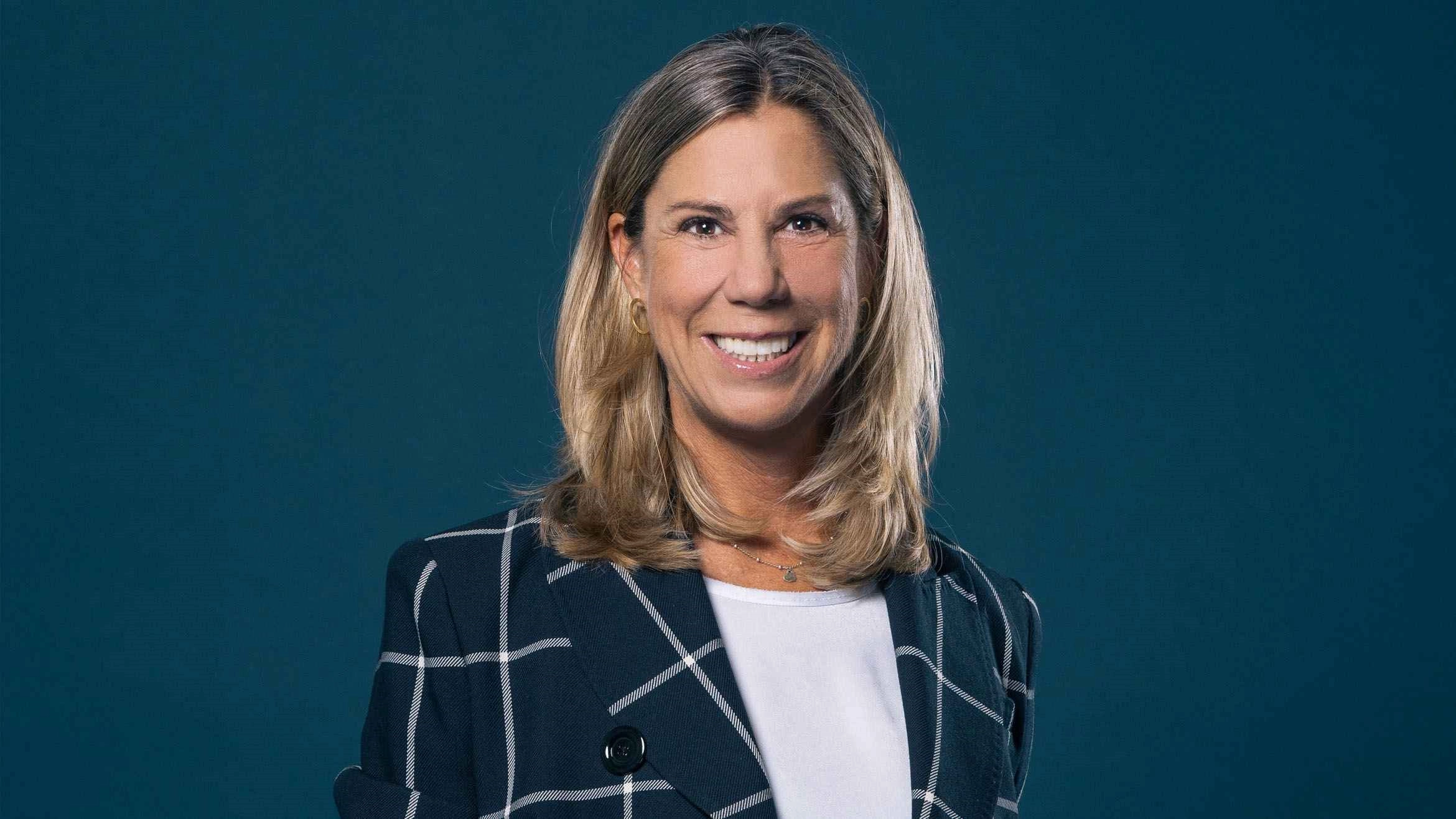 Professionelle Frau im karierten Blazer vor blauem Hintergrund, lächelnd und selbstbewusst.