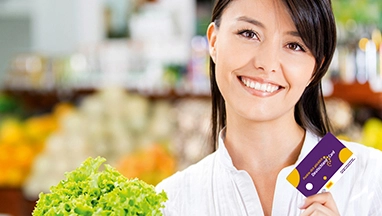 Lächelnde Frau mit Kundenkarte und frischem Salat im Supermarkt.