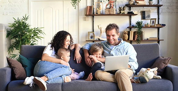 Familie entspannt auf Sofa mit Laptop, modernes Wohnzimmer, harmonische Atmosphäre.