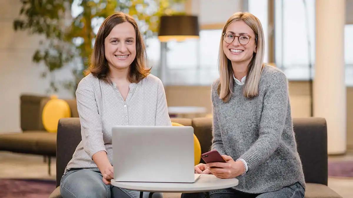 Moderne Teamarbeit im Büro: Zwei Frauen mit Laptop und Smartphone.
