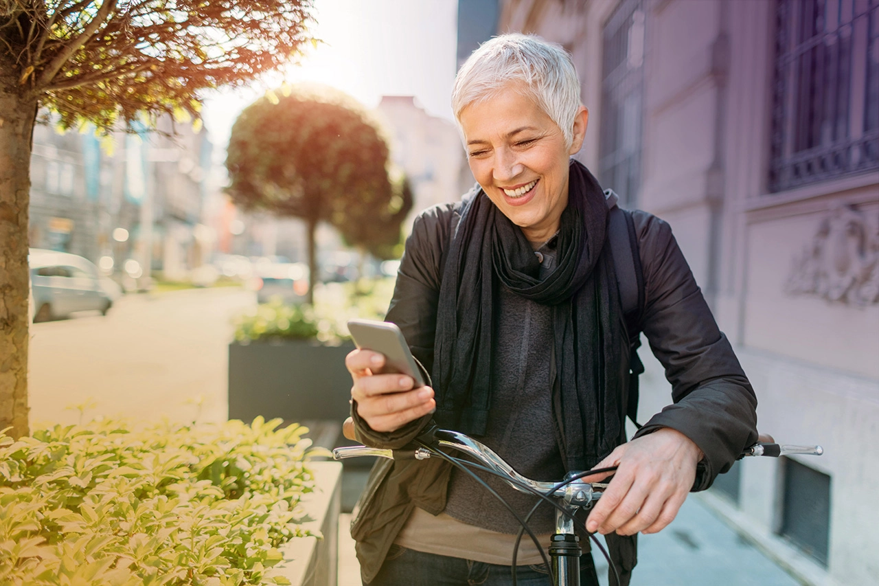 Ältere Frau genießt Stadtleben auf Fahrrad, lächelnd mit Smartphone. Urbaner Lifestyle.